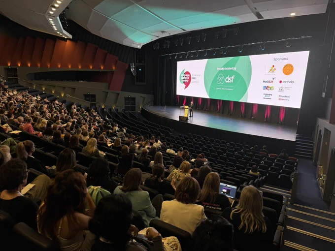Conference Hall with people sitting in seats with a big wide screen.