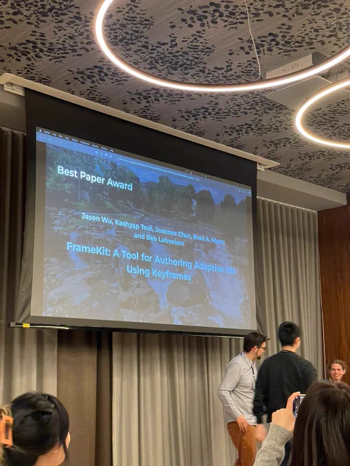 Jason is receiving an award for FrameKit at IUI. There is a projector screen that reads "Best Paper Award" with the authors of FrameKit and the full paper title.