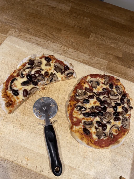 Pizzas on a shopping board with a pizza wheel cutter in the middle 