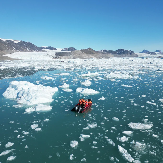 Drone shot of several people in a small boat navigating icy waters off Svalbard
