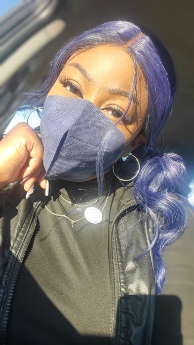 Masked Black lady in the car wearing a black shirt, necklace, earrings and a pin. 