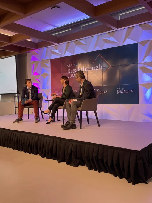 Three people sitting on stage talking with the STAT Breakthrough banner in the background.