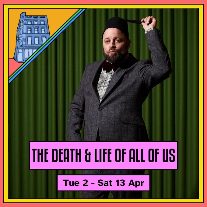 Text reads: "THE DEATH & LIFE OF ALL OF US, Tue 2 - Sat 13 Apr". Victor, a male performer, stands in front of a green curtain wearing a sharp, grey suit. He is wearing a lebanese hat with a tassle. He is holding the tassle in one hand with the other hand at his hip. He is pursing his lips provocatively.
