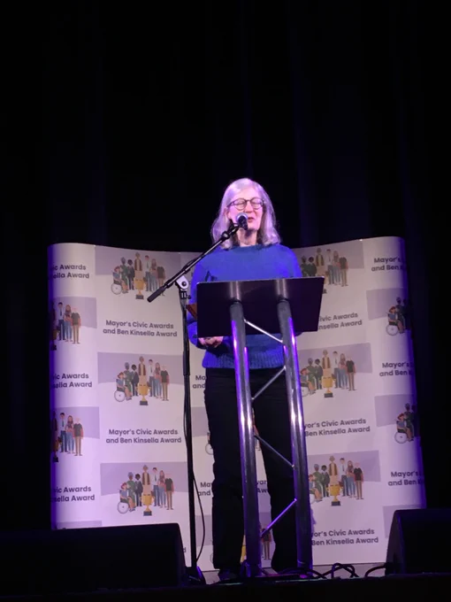 A female resident of Islington stands on a stage speaking at a silver podium under bright lights.