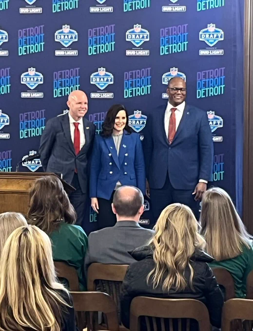 Visit Detroit President Claude Molinari, Michigan Governor Whitmer and Michigan Speaker of the House Joe Tate stand side-by-side in front of a backdrop that reads "Detroit, Detroit, Detroit. NFL Draft."