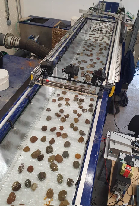 A photo of a flume with a white bed intermittently covered with pebbles. The  white bed is a scaled version of a reach of the River Greta.
