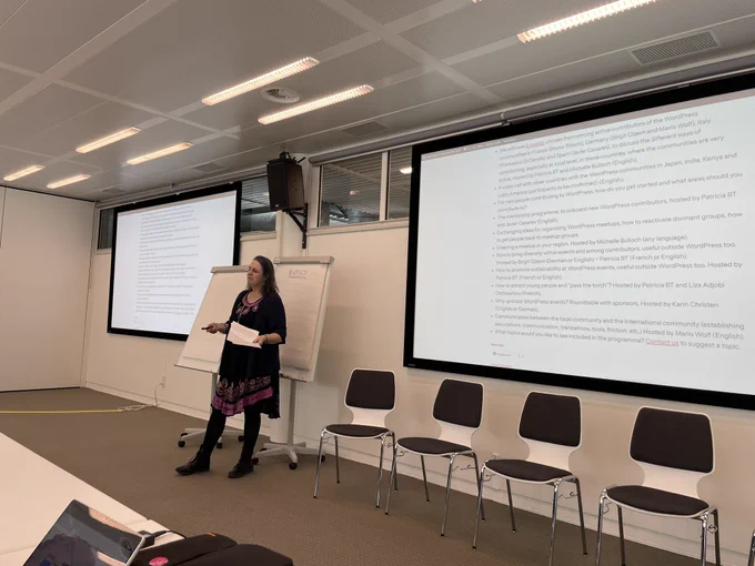 a middle aged woman standing before flipcharts and big screens in a conference room
