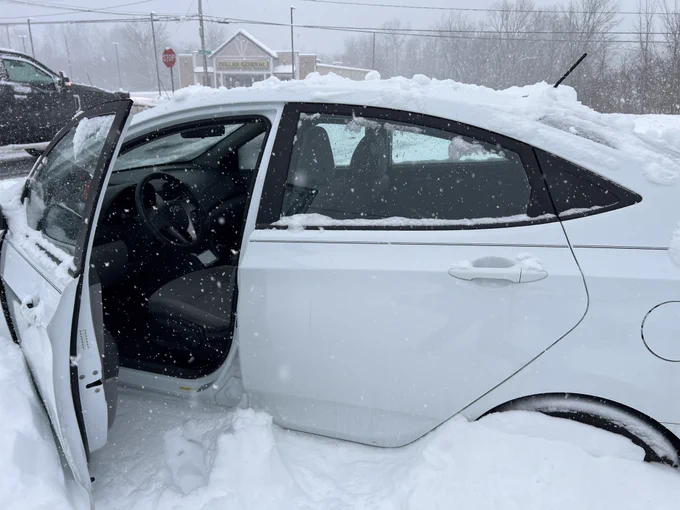 White car with driver side door open with snow around the car and snow up to tire height.