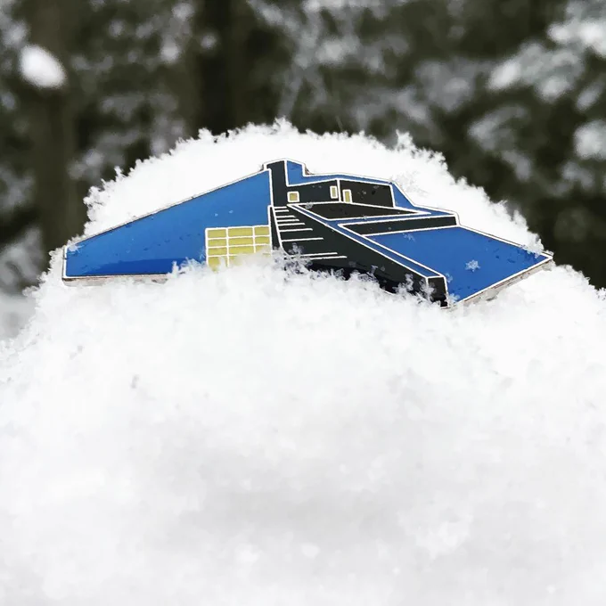 An enamel pin of a museum building in a snow bank