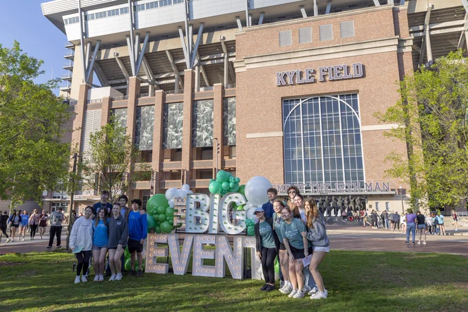 Students posing with a big event marquee in front of Kyle Field