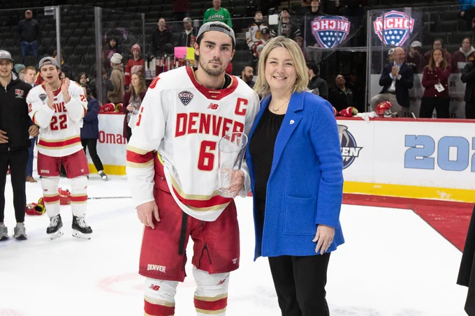 Denver captain McKade Webster holding the Most Outstanding Player award alongside NCHC Commissioner Heather Weems