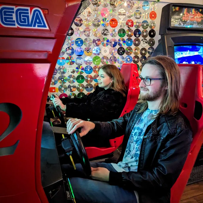 Two peeps playing Ferrari F355 Challenge, surrounded by a wall of compact discs
