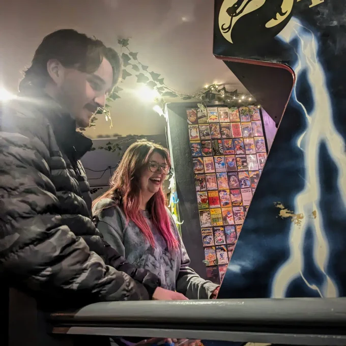 Two punters playing Mortal Kombat II. A wall of cassette games looms behind.