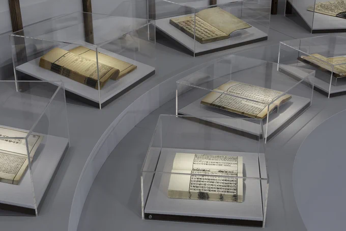 Display of aged books with Chinese characters housed in perspex boxes on grey plinth, with overhead lighting.