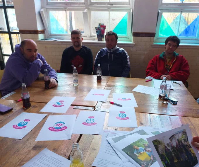 Four people sat at a large table covered with information leaflets about a Volunteering Hub project
