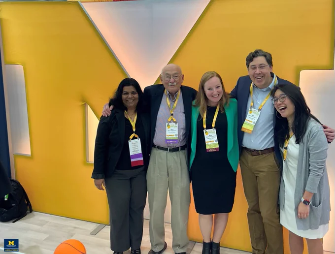 UMich Path faculty members Drs. Priya Kunju, Henry Appelman, Stephanie Skala, Evan Farkash, and Madelyn Lew pose in front of a "Block M" at the Mlabs booth at USCAP 2024.