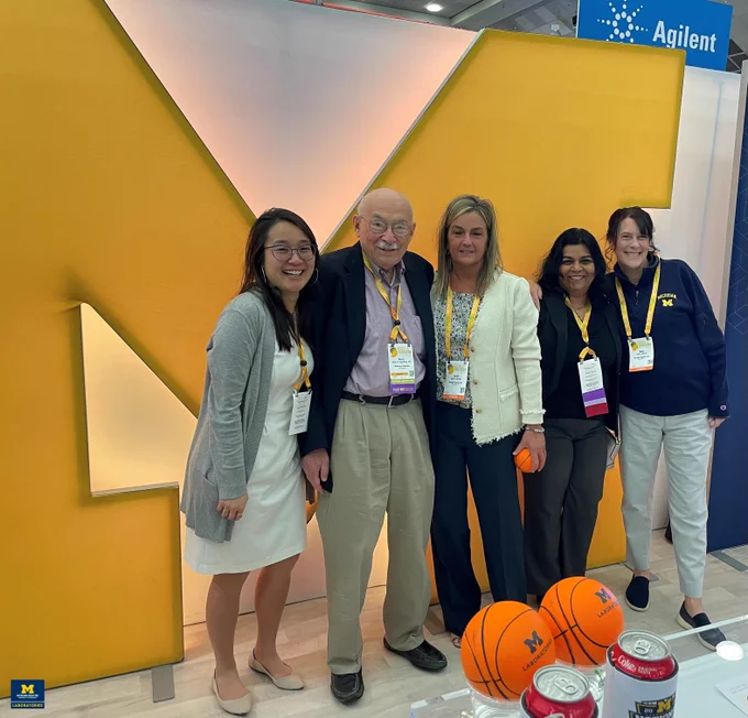 MLabs and UMich Path team members stand together in front of a "Block M" at the MLabs booth during USCAP 2024.