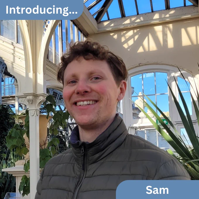 Photograph of Sam, indoors, with plants in the background
