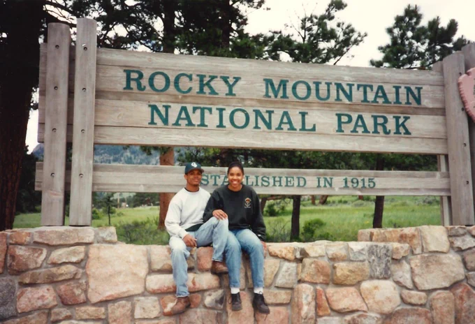 An older photo of Ronald and Zenarae Antione smiling next to the Rocky Mountain National Park sign. 