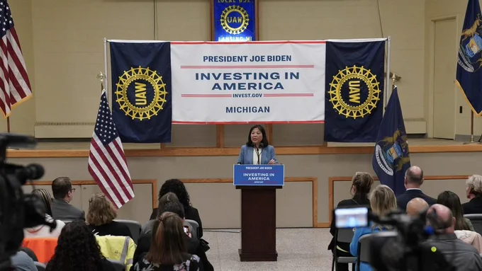 Acting Secretary of Labor Julie Su speaks at a podium with UAW banners and “President Joe Biden, Investing in America” signage.