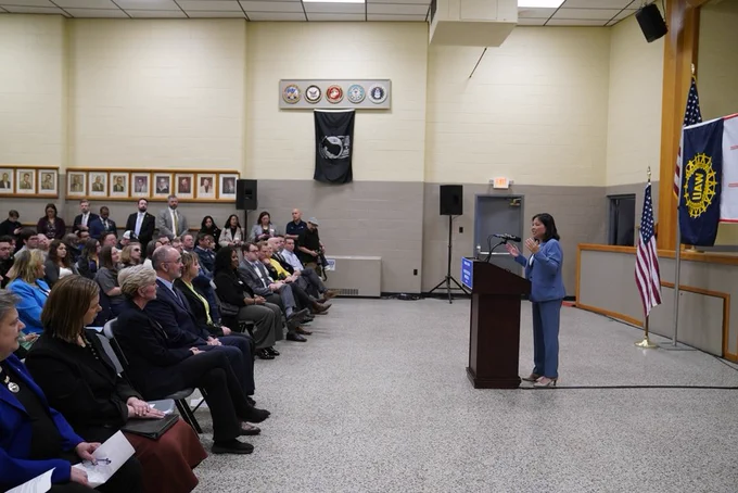Acting Secretary of Labor Julie Su speaks at a podium in front of a crowd. Rep. Slotkin, Secretary Granholm, UAW President Shawn Fain, and more are in the front row.