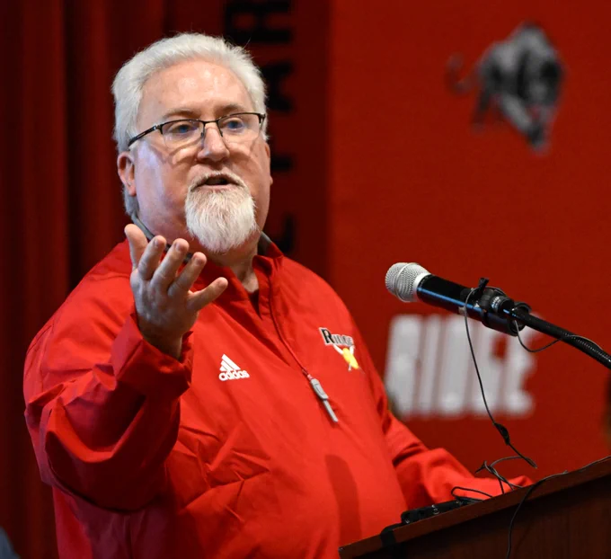 David McCoy stands at a microphone and speaks with his hand outstretched.