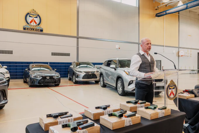 Man with cars in the background and firearms on the table.