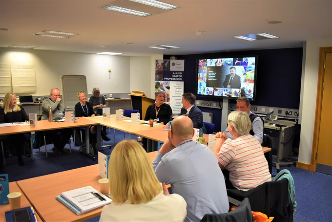 The Health Minister Robin Swann sits at a board table with Chief Allied Health Professionals Officer Michelle Tennyson and other AHP representatives.