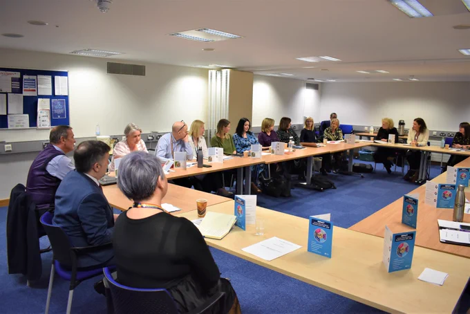 The Health Minister Robin Swann sits at a board table with Chief Allied Health Professionals Officer Michelle Tennyson and other AHP representatives.