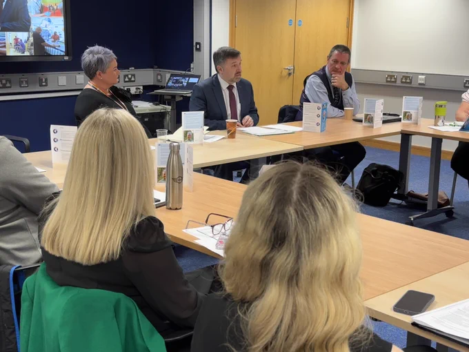 The Health Minister Robin Swann sits at a board table with Chief Allied Health Professionals Officer Michelle Tennyson and other AHP representatives.