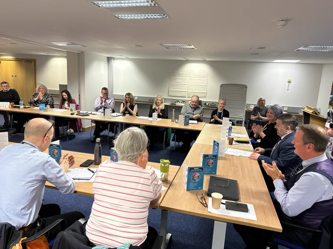 The Health Minister Robin Swann sits at a board table with Chief Allied Health Professionals Officer Michelle Tennyson and other AHP representatives.