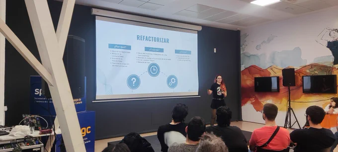 Vemos a María Guerra exponiendo delante de personas, con un proyector que muestra una imagen con los pasos de la refactorización (por qué, cuándo y cómo)