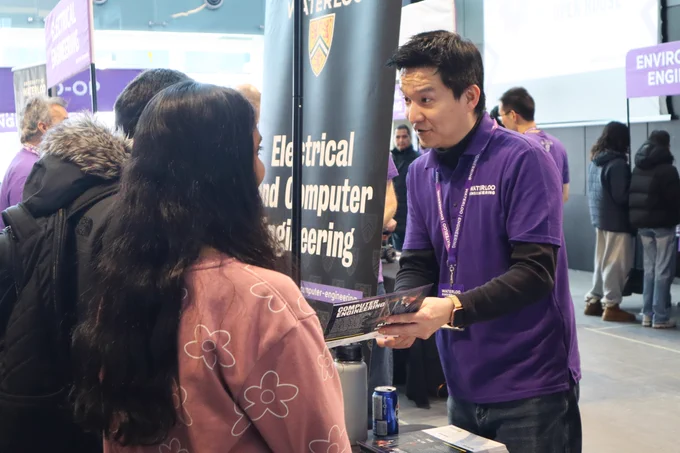 Photo of a volunteer explaining and pointing at the Computer Engineering brochure to the visitors.