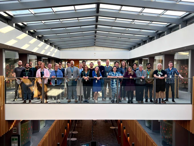 A group of over 25 people pose for the photo on bridge connecting two sides of an office building.