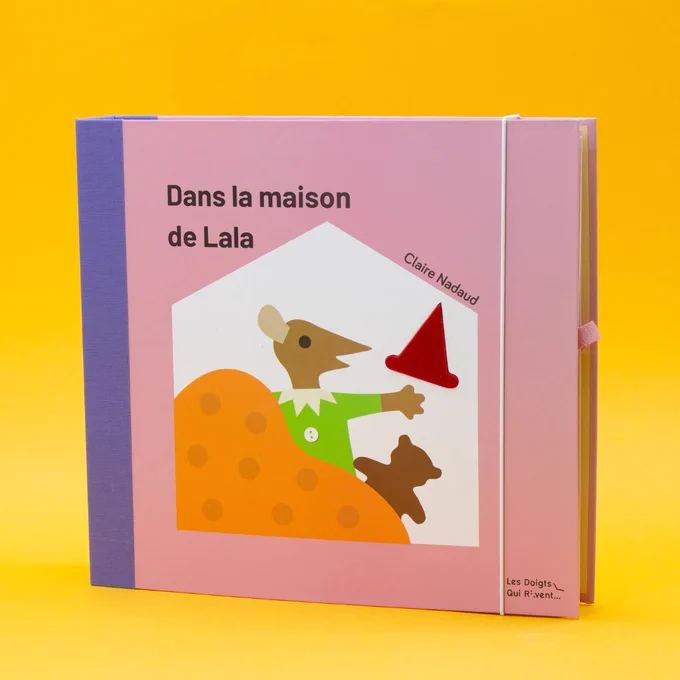 couverture du livre dans la maison de Lala, dos toilé et tenu par un élastique, sur la couverture Lala la souris est représentée entourée d'objets : couverture, oursons, chapeau. le chapeau texturé est inséré dans la couverture.
