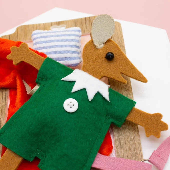 zoom sur le personnage de lala la souris sur son lit, elle est fabriquée en feutrine avec deux yeux rond et un pyjama vert avec un col blanc et un bouton blanc cousus sur le ventre