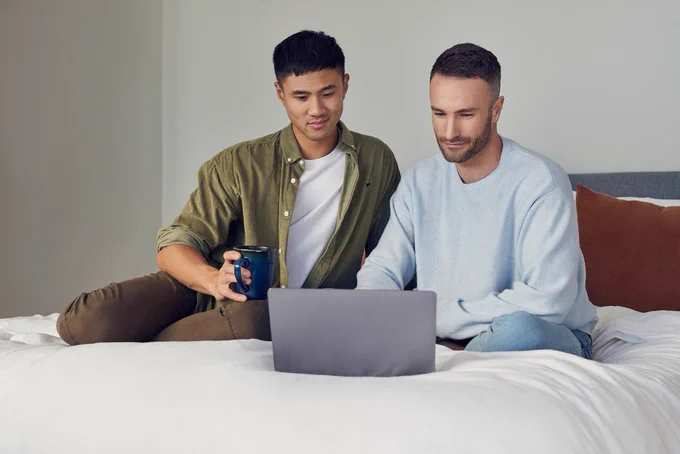 Twee mannen op een bed kijken naar een laptop.