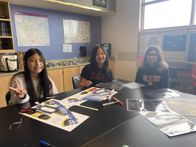 three students sitting at a desk in a classroom