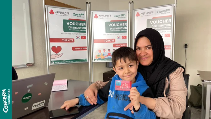 Female beneficiary and her son posing for the camera holding a market card
