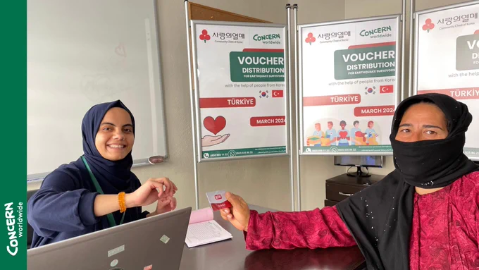 Concern Staff and Beneficiary posing for the camera holding a market card.