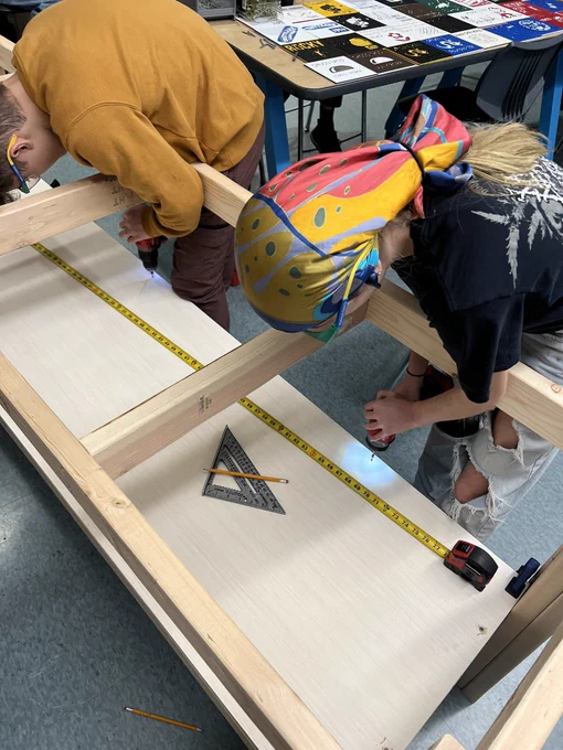 Two students drilling holes and fastening the bottom shelf to the workbench