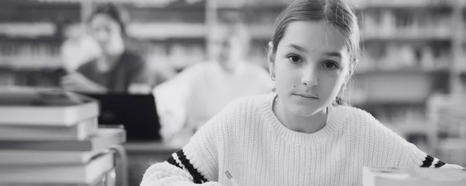 Young girl student in library, staring at camera, looking serious
