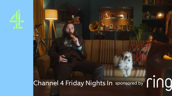 Joe Wilkinson eating an ice lolly on his sofa. He is sitting next to a terrier dog as part of Ring's advert.