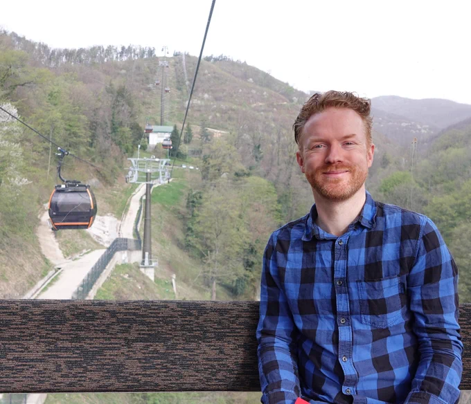Phil sat on a bench in a cable car cabin, going up a hill, with other cable cars in the distance