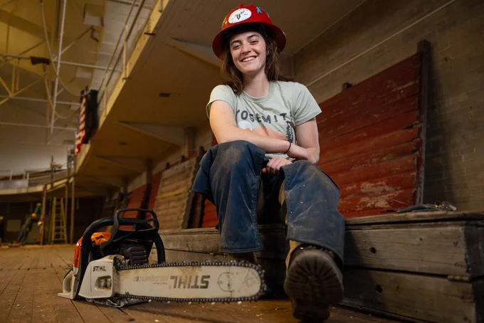 Photo of University of Montana Truman Scholar Jaiden Stansberry as she sits on the ground in a hard helmet with a chainsaw