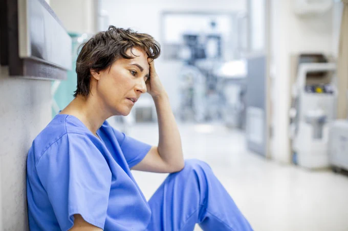 Photo of a tired female  doctor sitting on the floor in a hospital.