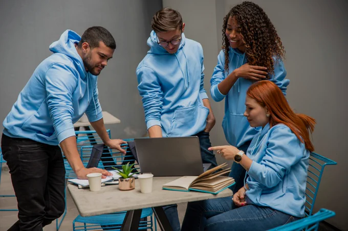 Four people in light blue sweatshirts around a rectangular table with a computer, book, notebooks, small succulent plant and two coffee cups in an office setting

In collaboration with Pablo Merchán Montes
https://unsplash.com/@pablomerchanm
