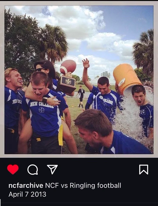 Null Sets, wearing Four Winds on their blue uniforms, celebrate victory over Ringling College.  On one side, a cooler of ice is getting dumped over someone. In the center, a hand holds a trophy aloft. 