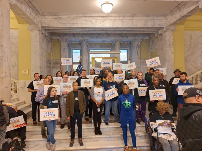 A group of people stand on steps inside the Wilson Building before the mayor's budget proposal.