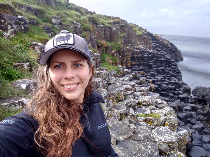 Amy Wilson in a black rain coat standing at the Giants causeway in Northern Ireland. 